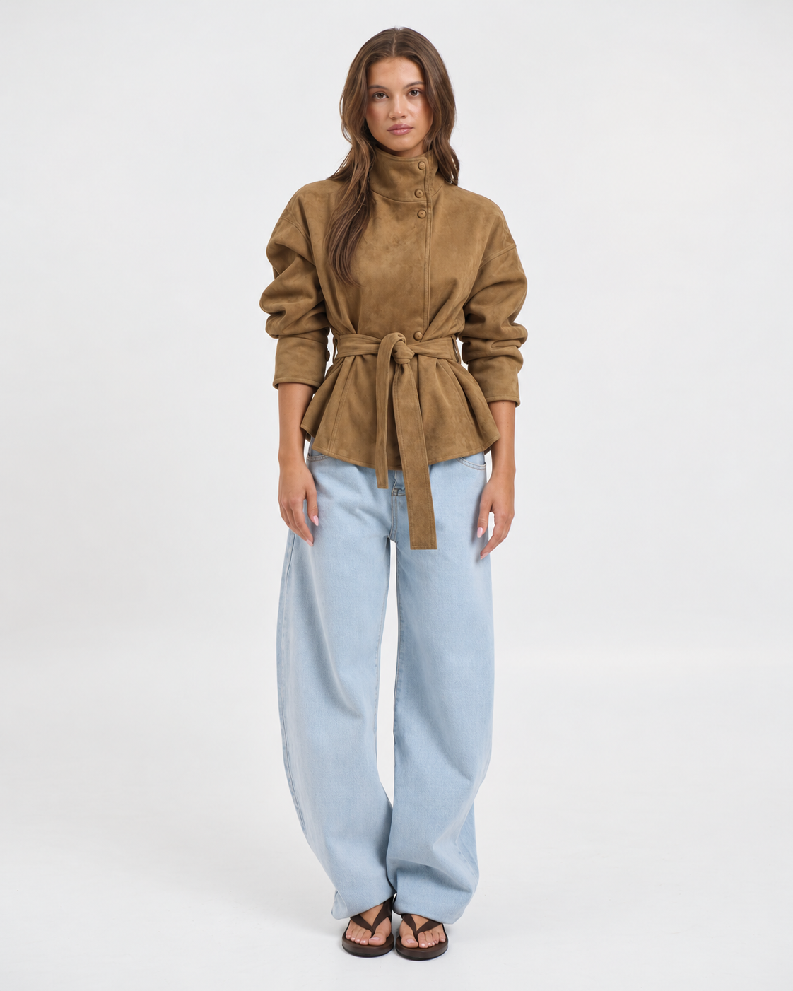 Donna che indossa la Giacca Vittoria con Collo Alto e Cintura in beige, abbinata a jeans a gamba larga chiari, vista frontale.